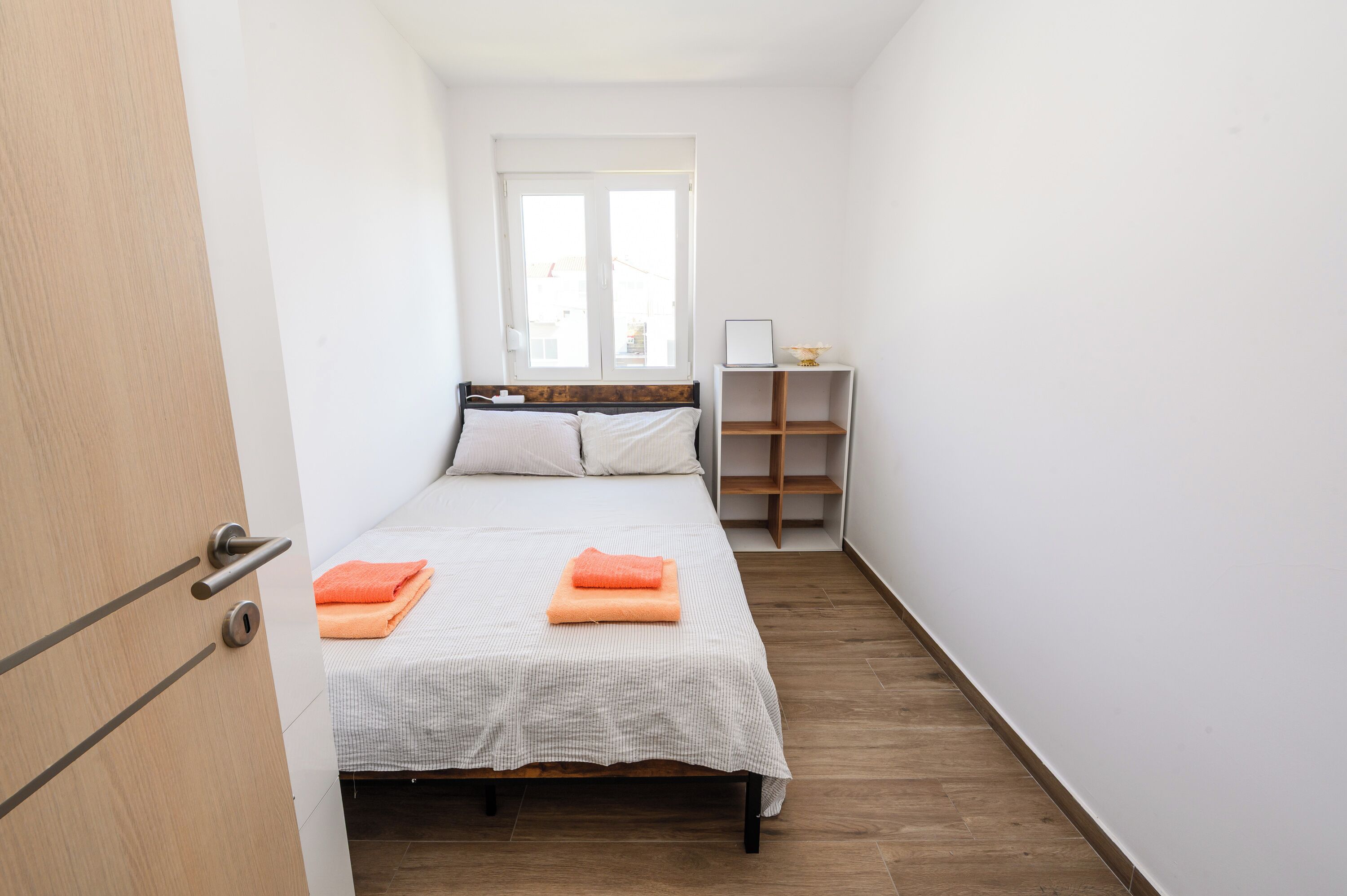 A narrow room with a bed, a window, and a small shelf with a lamp.
