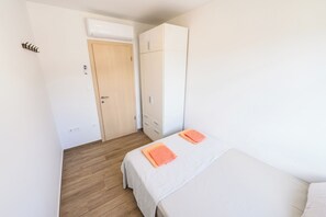 Ein Schlafzimmer mit einem Bett, zwei orangefarbenen Handtüchern, einem Kleiderschrank, Holzboden und einer Tür mit Klimaanlage.