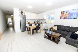 Eine moderne Küche mit weißen Schränken, einem Esstisch mit Stühlen, einem schwarzen Sofa und einem Bild an der Wand.