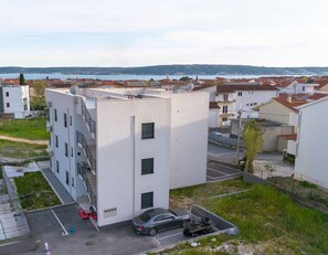 A multi-story residential building with a parking area and a view of a body of water in the background. - Condo with 2 bdr and parking (Kaštel Stari)