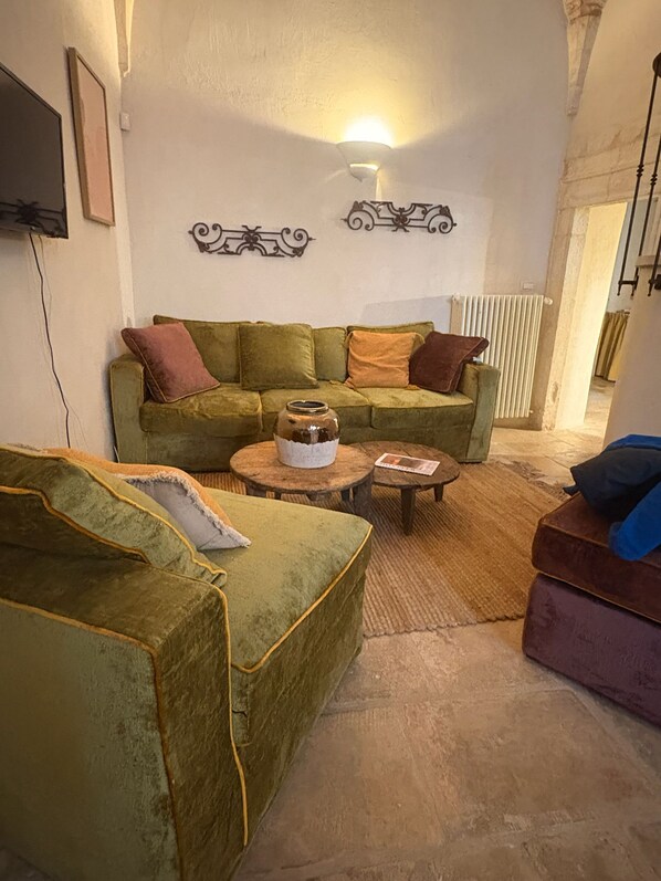 Ein Wohnzimmer mit einem grünen Sofa, einem kleinen runden Tisch und einem gemusterten Teppich.