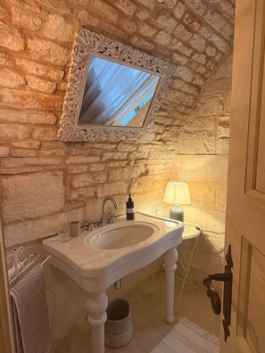 Ein Badezimmer mit Steinwand, Waschbecken in Weiß, Spiegel und Lampe.