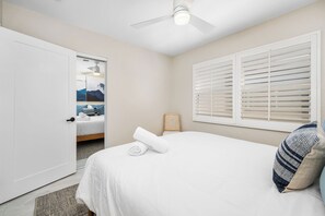 Ein Hotelzimmer mit einem Bett, einem Deckenventilator, einem Fenster mit Jalousien und einer Tür zu einem anderen Raum.