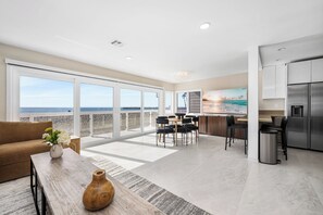 Eine moderne Küche mit einem Edelstahlkühlschrank, eine Essecke mit Tisch und Stühlen sowie große Fenster mit Blick auf den Strand.