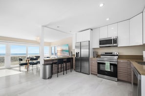 A modern kitchen with stainless steel appliances, a large island, and a view of the beach. - Steps to Sand Oceanfront Getaway (Seal Beach)