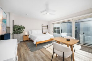 A modern bedroom with a bed, bedside table, and a desk with a chair. - Beachfront Studio Steps to Main Street (Seal Beach)
