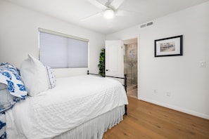 A bedroom with a bed, a window with blinds, a door leading to a bathroom, and a framed picture on the wall. - Classic Balboa Island Coastal Escape (Newport Beach)