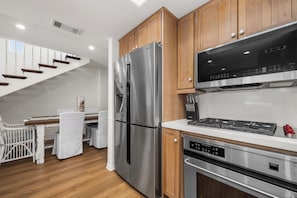 A modern kitchen with stainless steel appliances, wooden cabinets, and a white staircase. - Classic Balboa Island Coastal Escape (Newport Beach)