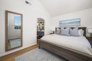 Een slaapkamer met een groot bed, een spiegel, een schilderij en een badkamer zichtbaar via een boog.