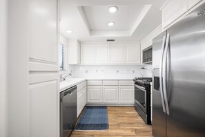 A compact kitchen with white cabinetry, stainless steel appliances, and a wooden floor. - Coastal Living on Balboa Island (Newport Beach)