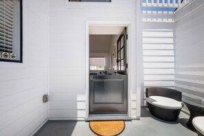 A narrow entryway with a door leading to a kitchen area, a wicker chair, and a small outdoor seating area. - Coastal Living on Balboa Island (Newport Beach)