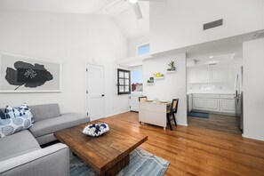 A modern living room with a wooden coffee table, grey sofa, and a dining area with a white table and chairs. - Coastal Living on Balboa Island (Newport Beach)