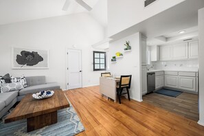 A modern living room with a sofa, coffee table, and a dining area with chairs. - Coastal Living on Balboa Island (Newport Beach)