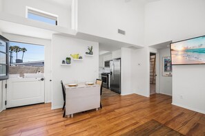 A modern kitchen with white cabinets, a stainless steel refrigerator, and a dining area with a wooden table and chairs. - Coastal Living on Balboa Island (Newport Beach)