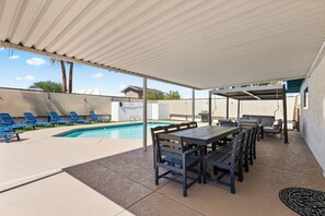 Een terras buiten met een zwembad, lounge stoelen, een tafel met stoelen en een barbecue.