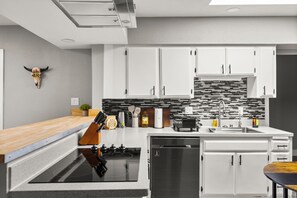 Eine moderne Küche mit weißen Schränken, einer schwarzen Induktionskochplatte, einem Edelstahlkühlschrank und einer Spritzschutzwand mit schwarz-weißen Fliesen.