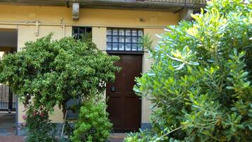 Een gebouw met een bruine deur, een raam met een rasterpatroon en een balkon met hangplanten.