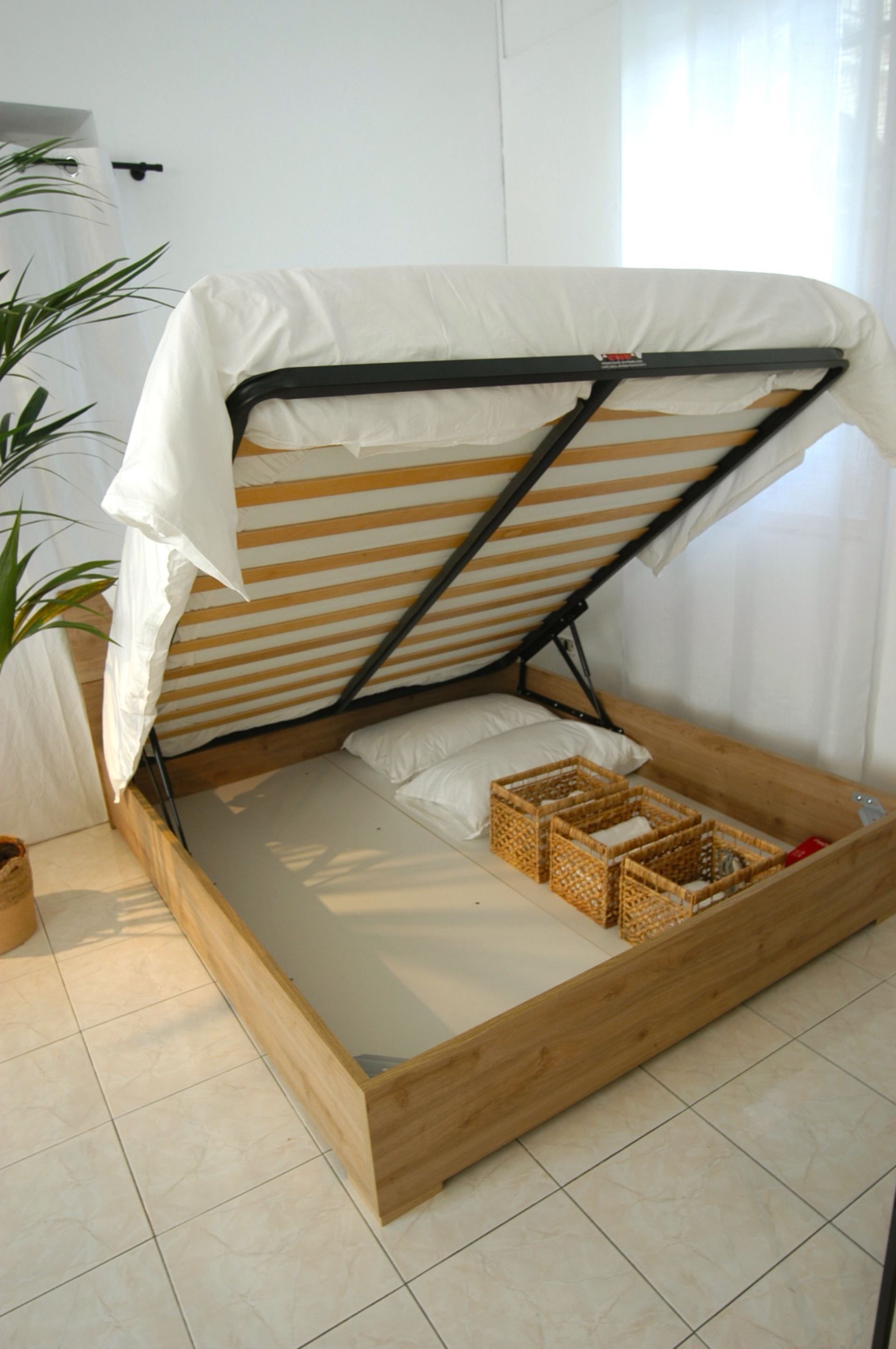 A compact bed with a wooden frame and a white mattress, accompanied by a small bedside table and a potted plant.