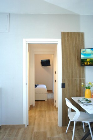 A hotel room with a bed, a TV mounted on the wall, a wooden panel wall, and a dining area with a table and chairs. - Dimora Romana – MARTINI's Home, Milano (Milano)