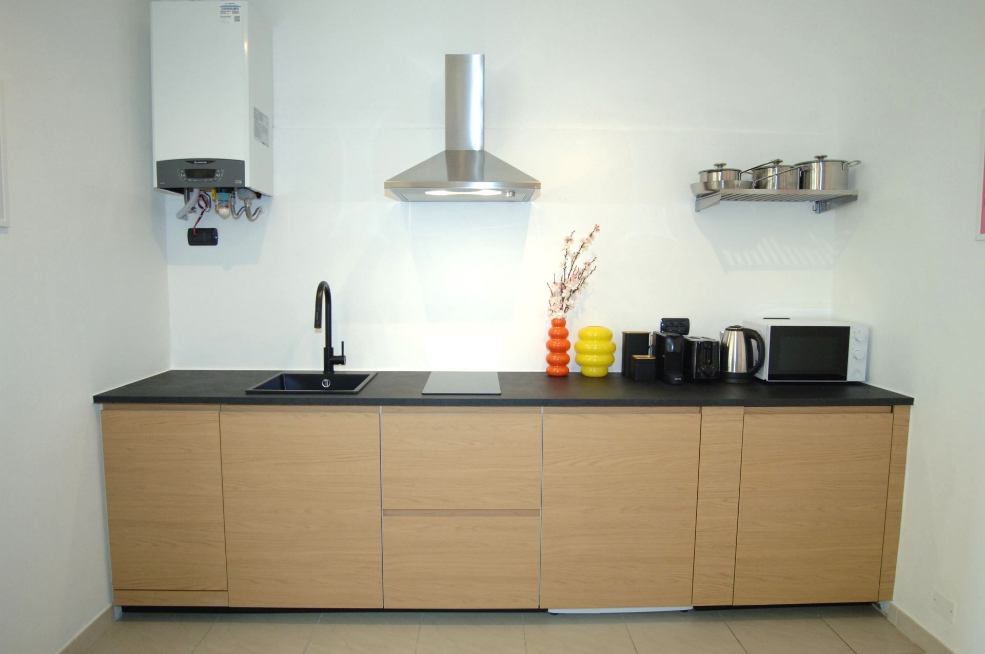 A modern kitchen with a black countertop, a stainless steel range hood, a built-in sink, and a microwave.