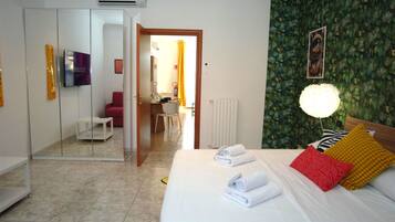 Habitación de hotel con cama, televisión, espejo, baño y puerta que da a un pasillo.