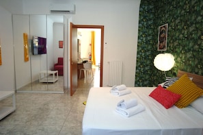 A hotel room with a bed, a television, a mirror, a bathroom, and a door leading to a hallway. - Ecletic Jungle - MARTINI'S home (Milano)