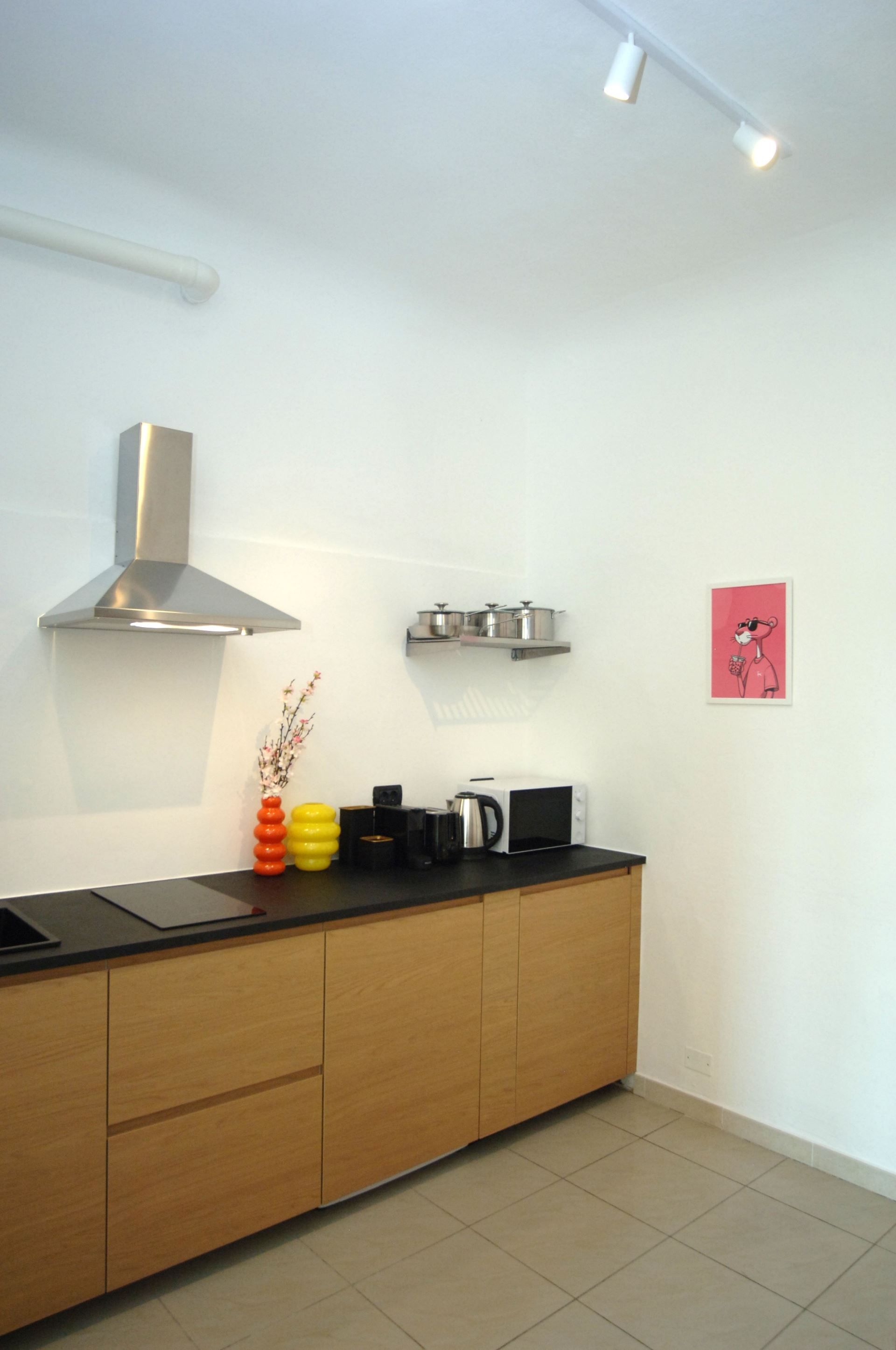 A modern kitchen with a stainless steel range hood, a microwave, and a kettle on the countertop.