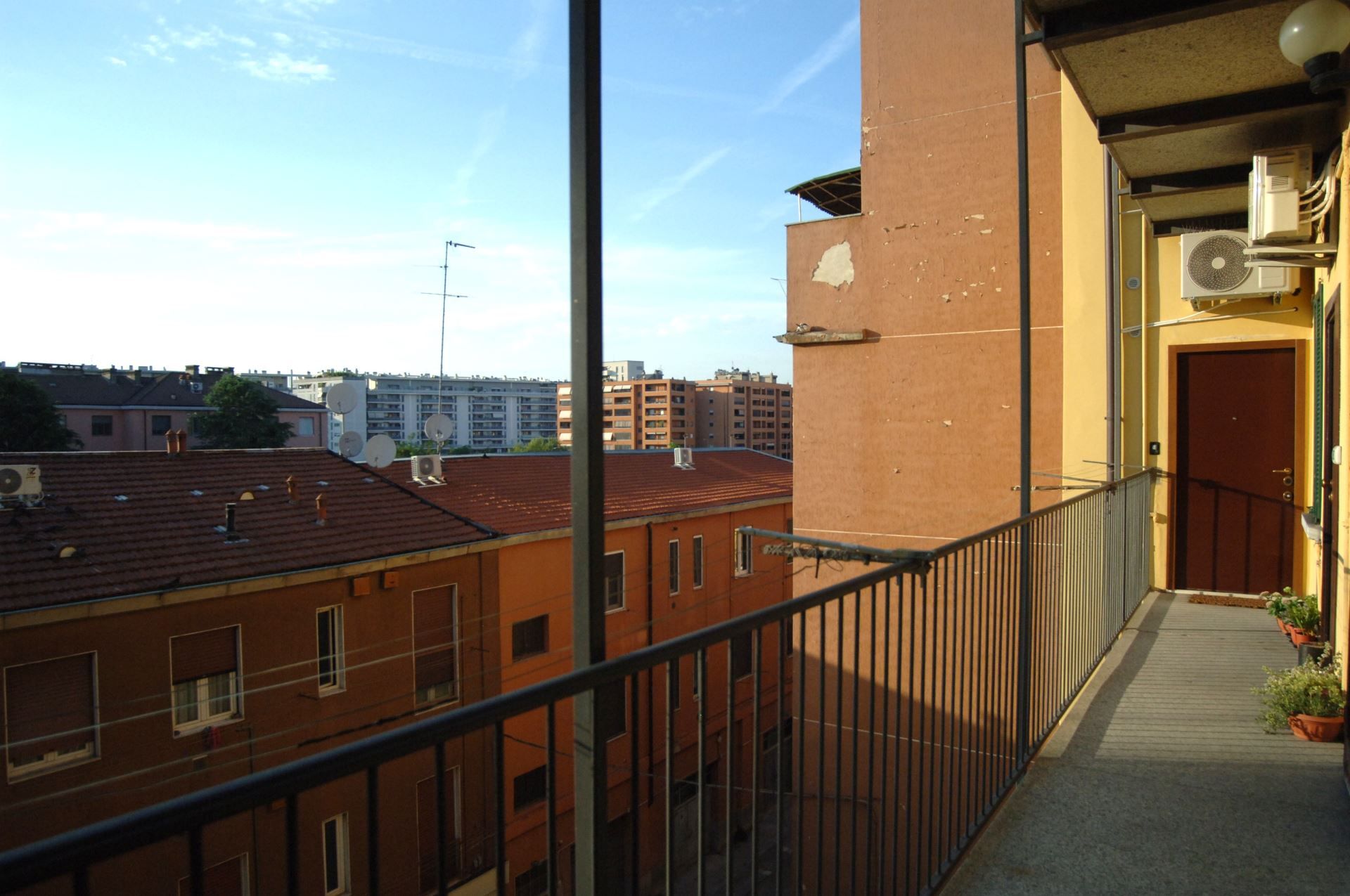 Un balcone con ringhiera in metallo che si affaccia su una veduta urbana con numerosi edifici.