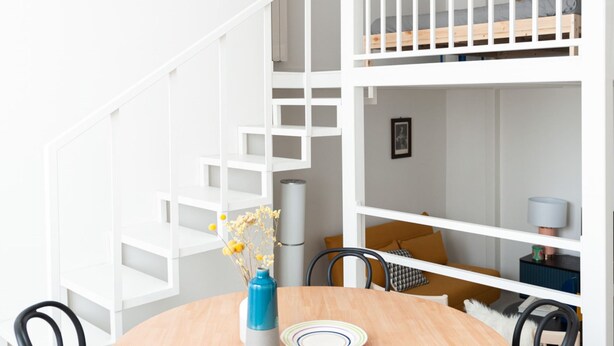 A modern interior with a round wooden table, black chairs, a white staircase, and a bunk bed in the background. - Foresteria MILO MARTINI's Home (Milano)