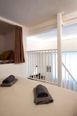 A hotel room with a bed, a window with curtains, a view of the outside, and a staircase. - Foresteria MILO MARTINI's Home (Milano)