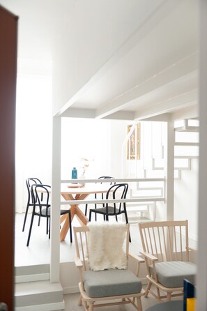 A modern dining area with a wooden table and chairs, a white interior, and a staircase leading to another level.