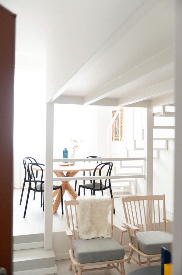 Un comedor moderno con mesa y sillas de madera, interior blanco y una escalera que sube a otro nivel.