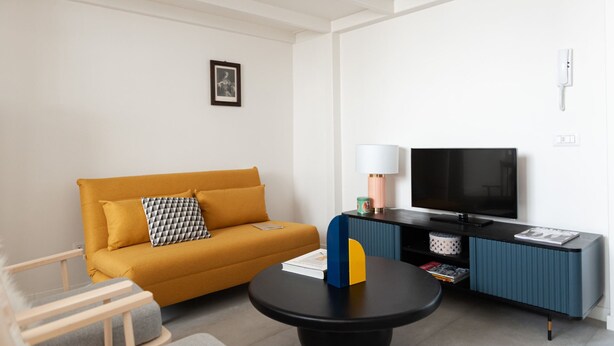 En moderne stue med sofa, sofabord, fjernsyn og lampe.