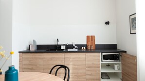 A modern kitchen with a black countertop, wooden cabinets, a sink, a microwave, and a cutting board. - Foresteria MILO MARTINI's Home (Milano)