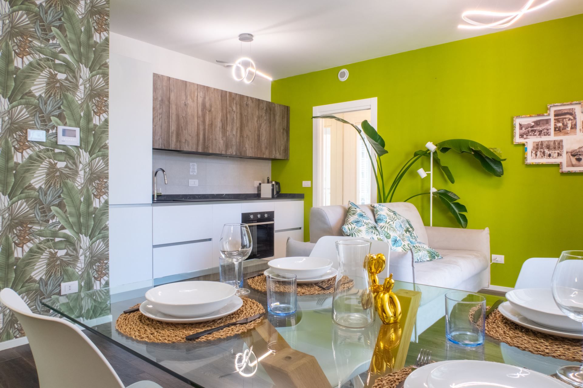 Una cucina moderna con mobili in legno, un'area pranzo con tavolo in vetro e una parete verde brillante.