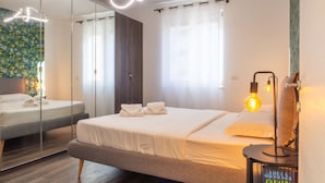 Ein modernes Hotelzimmer mit einem großen Bett, einem Nachttisch mit Lampe, einem Spiegel und Blick ins Freie.