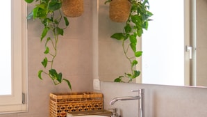 Ein Badezimmer mit einem weißen Waschbecken, einer Holz-Waschkommode, einem Spiegel und zwei Hängekörben mit Grünpflanzen.