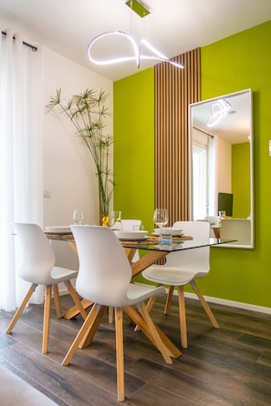 A modern dining area with a glass table, white chairs, and a green accent wall. - Green Apartment by MARTINI's Home (Milano)