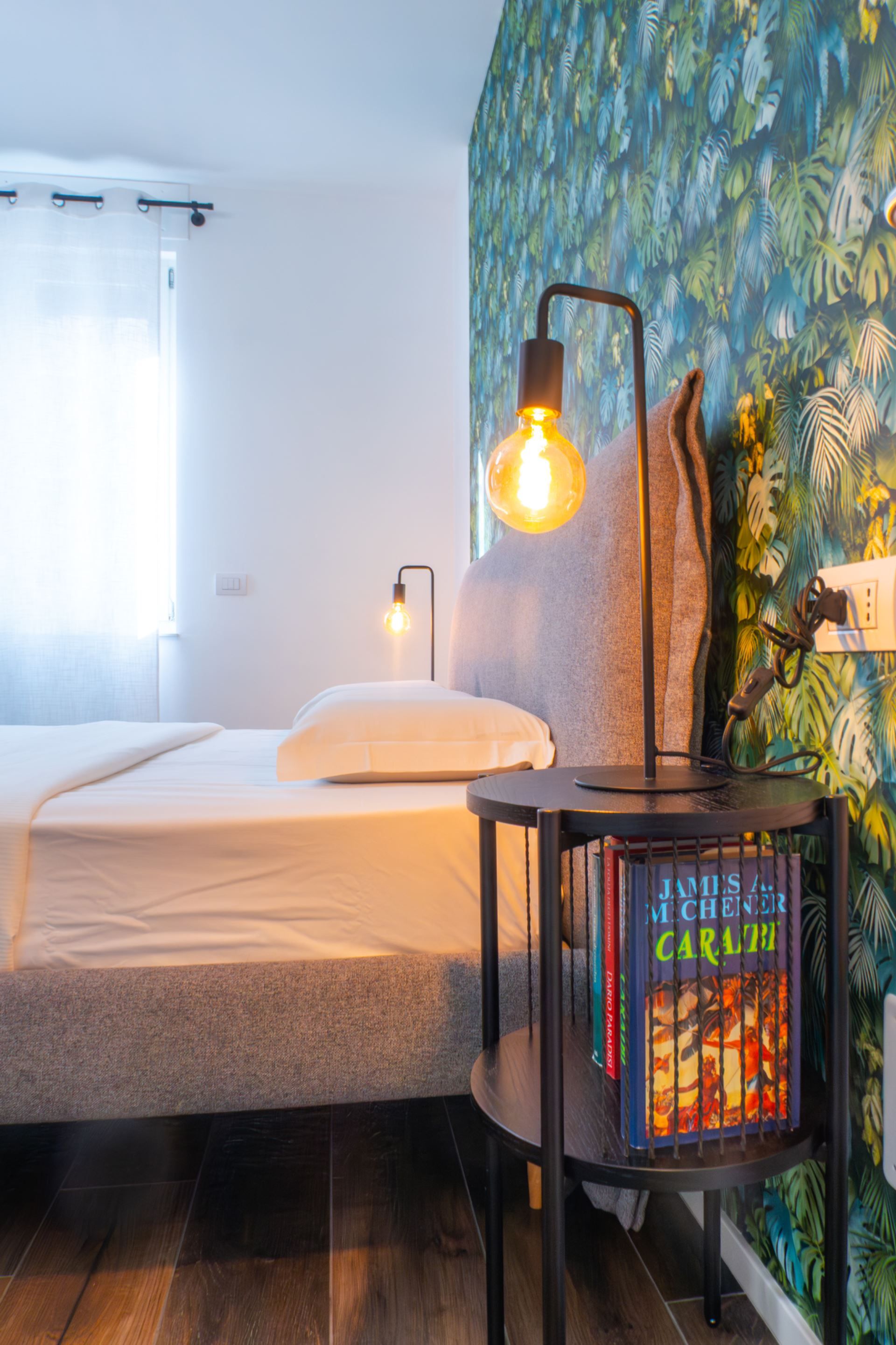 A hotel room with a bed, a nightstand with a lamp, and a bookshelf.