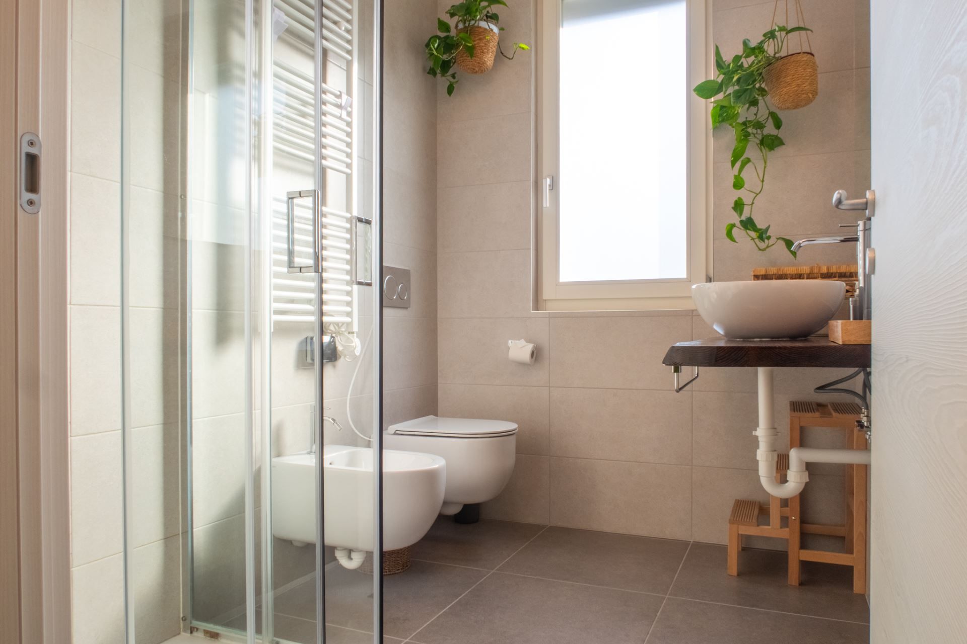 Une salle de bain avec une douche à parois de verre, des toilettes, un lavabo avec un plan de travail en bois et deux plantes suspendues.