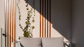 A modern outdoor seating area with a white sofa and a small table, set against a wall with vertical wooden slats and a climbing plant.