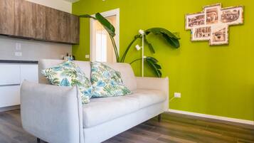 A living room with a sofa, a green wall, and a kitchen in the background.