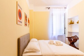 A hotel room with a bed, pillows, a headboard, a wooden chair, a shelf with decorative items, and a window with curtains. - Jasmine House - MARTINI's Home, Milano (Milano)