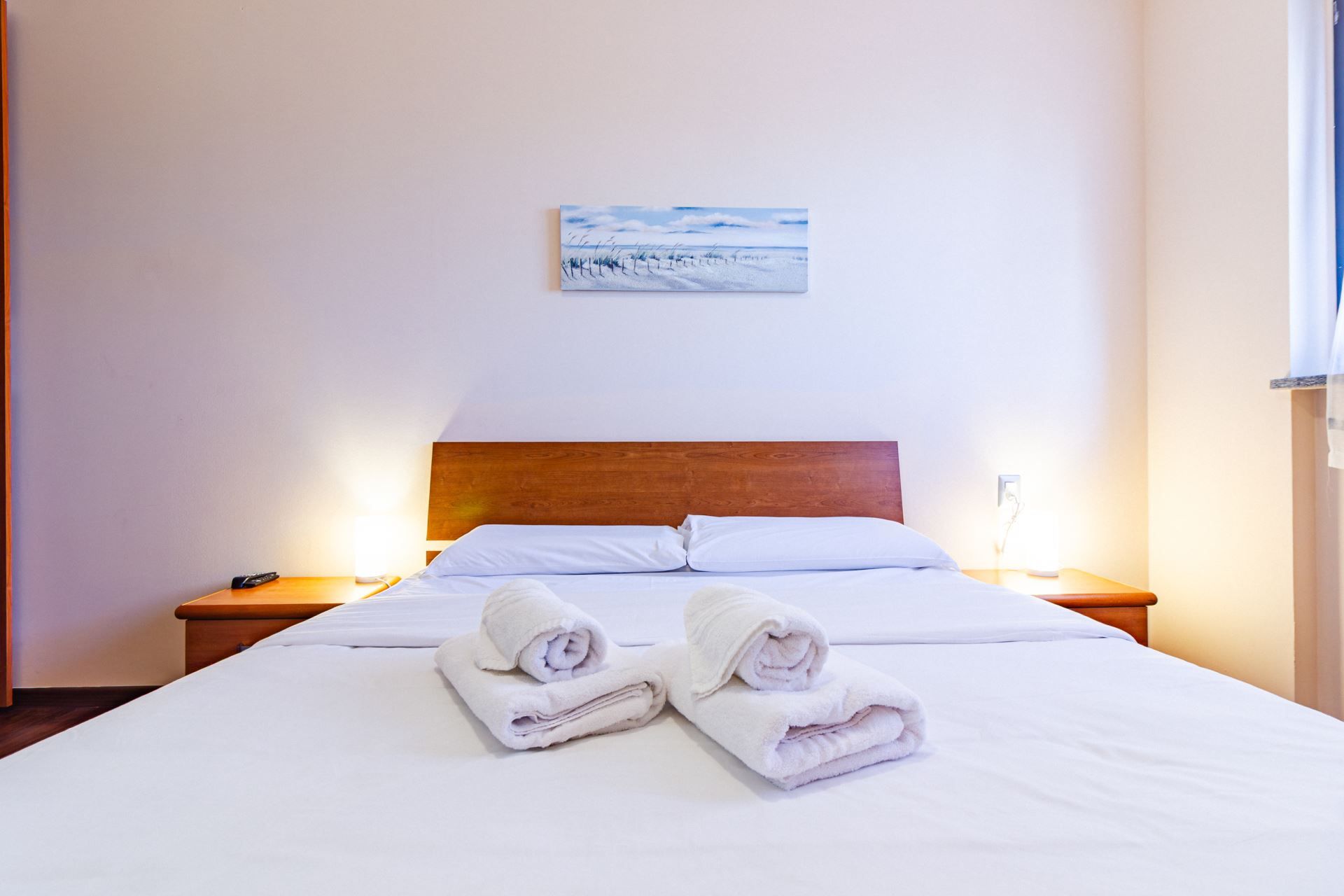 Una camera d'albergo con un letto, due comodini, un tavolino e un quadro appeso al muro.