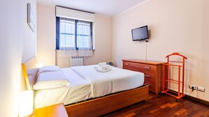 Een hotelkamer met een bed, een televisie, een houten dressoir en een rode bagagekar.