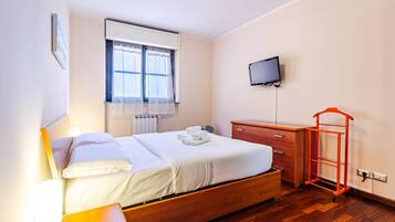 A hotel room with a bed, a television, a wooden dresser, and a red luggage cart.