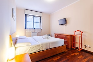 Una habitación de hotel con una cama, televisión, cómoda de madera y un carrito para equipaje rojo.