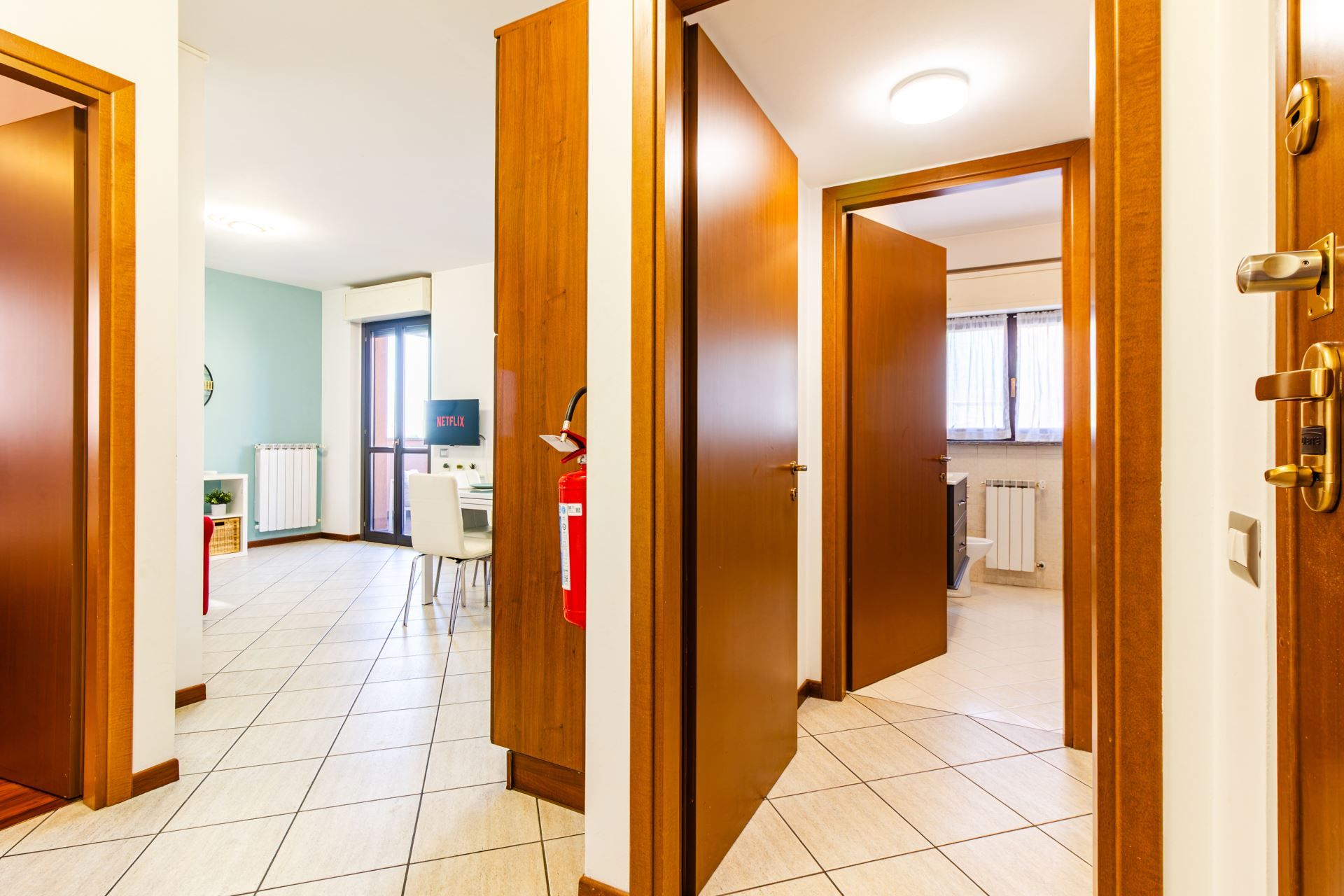 Un corridoio con porte in legno che conducono a una stanza con una scrivania, una sedia e un televisore che mostra 'NETFLIX'.