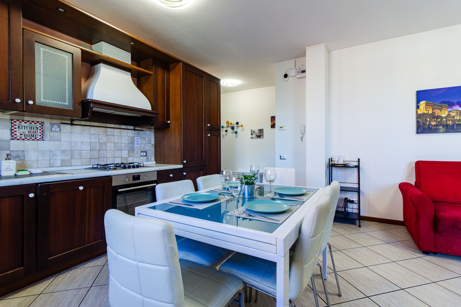 A modern kitchen with a dining area, white chairs, and a red armchair.
