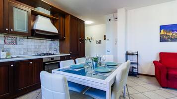 A modern kitchen with a dining area, white chairs, and a red armchair.